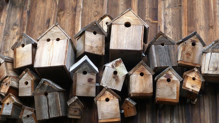 Flera träfärgade fågelholkar i olika storlekar som sitter tillsammans på en vägg. Skall symbolisera samlingen av bostadsrätter i en bostadsrättsförening.