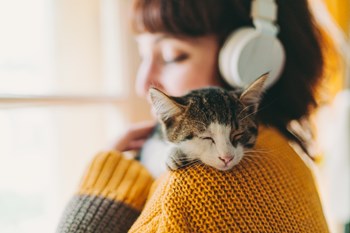 Ung kvinna med hörlurar och katt på axeln som symboliserar den lugn och trygghet som man kan känna i sitt nya hem